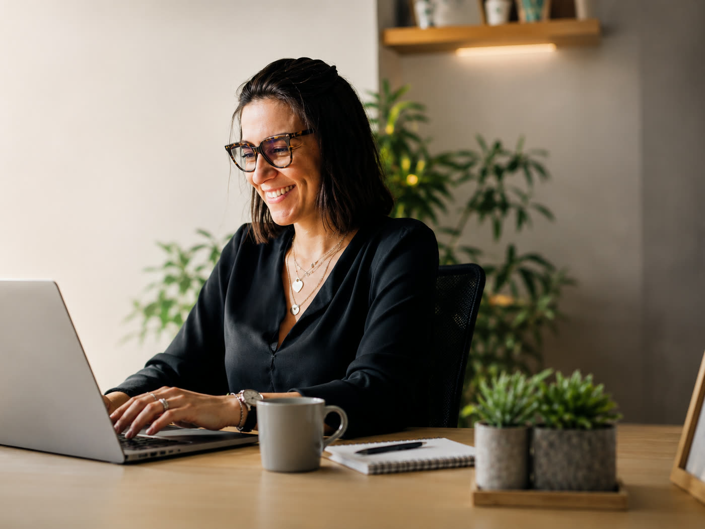Mulher sorrindo enquanto trabalha no notebook em um escrit&oacute;rio claro e organizado